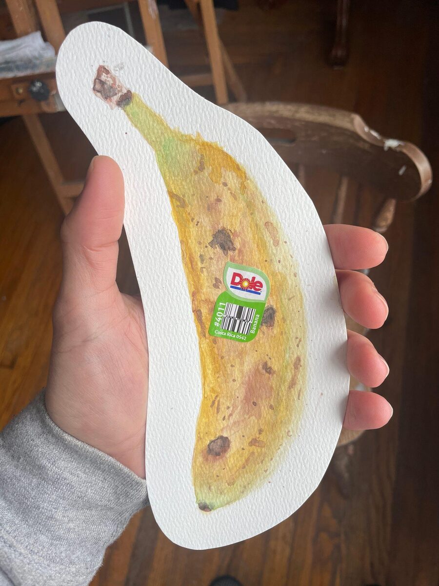 A watercolor-painted paper banana held in hand